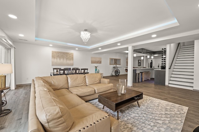 living room with a tray ceiling, recessed lighting, wood finished floors, and a chandelier