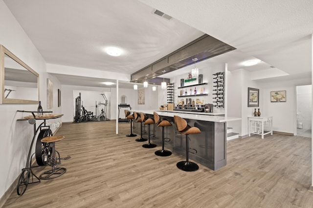 bar with a bar, light wood-style floors, visible vents, and a textured ceiling