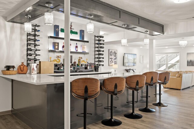 bar featuring beamed ceiling, wet bar, wood finished floors, and hanging light fixtures