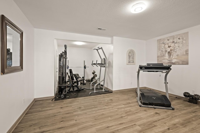 exercise room featuring visible vents, a textured ceiling, light wood-type flooring, and baseboards