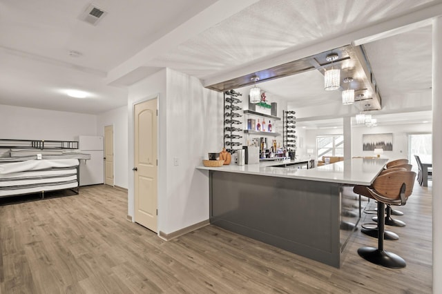 bar with light wood finished floors, visible vents, baseboards, freestanding refrigerator, and a bar