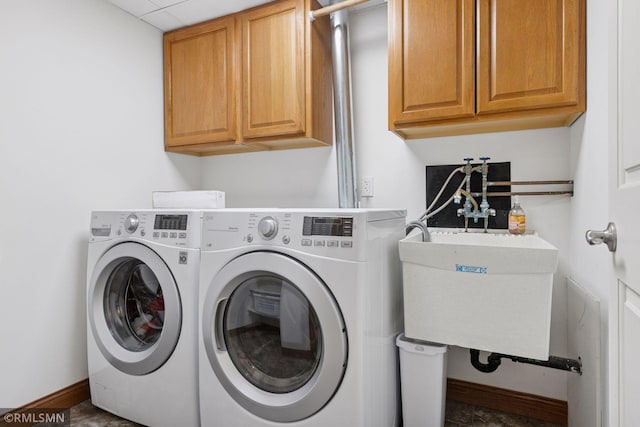 washroom featuring washing machine and dryer, cabinet space, a sink, and baseboards