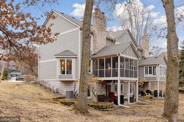 back of house featuring central AC unit, a sunroom, a chimney, roof with shingles, and a patio area