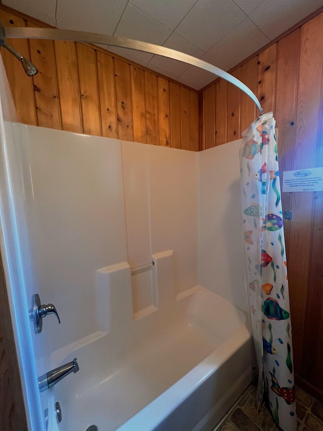 bathroom featuring wood walls, a drop ceiling, and shower / tub combo with curtain