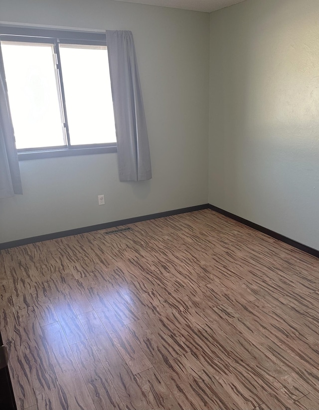 spare room with wood finished floors, visible vents, and baseboards