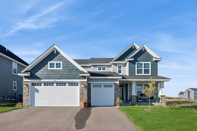 craftsman-style house with aphalt driveway, a porch, a garage, stone siding, and a front lawn