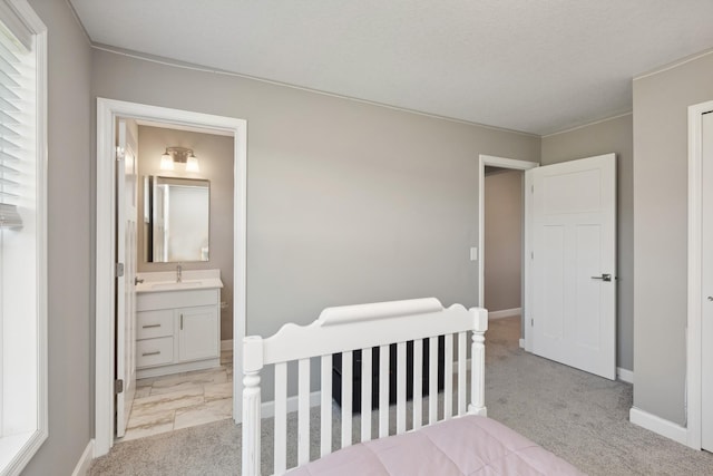 bedroom with baseboards, ensuite bath, a sink, and light colored carpet