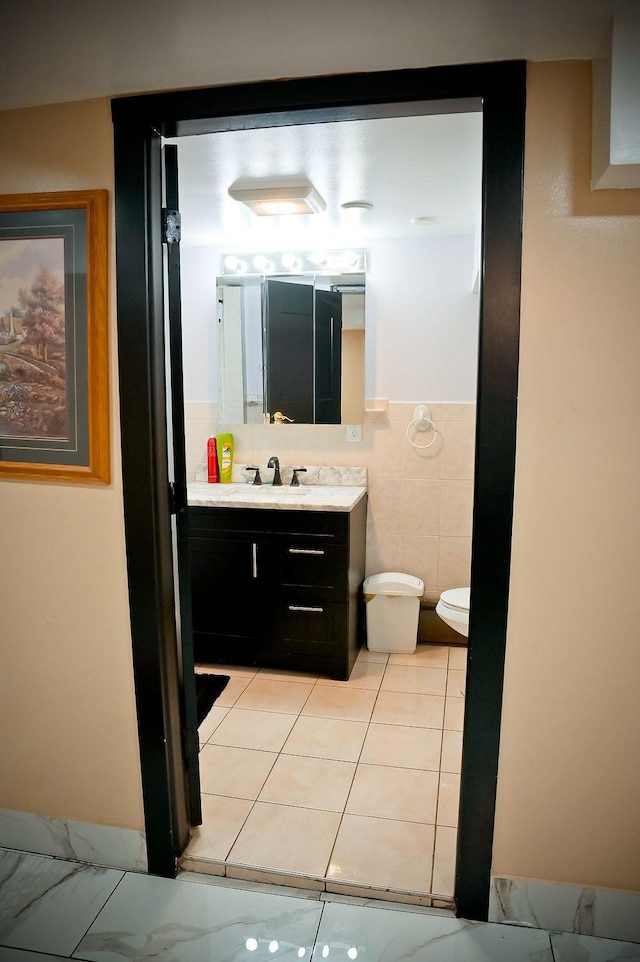 bathroom featuring wainscoting, toilet, tile patterned flooring, vanity, and tile walls