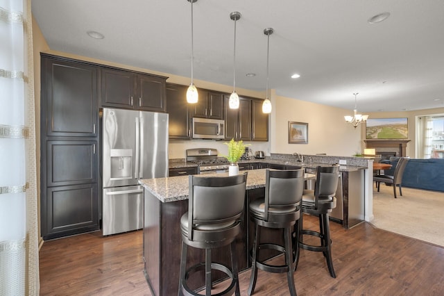 kitchen with stainless steel appliances, dark wood finished floors, a kitchen bar, and light stone countertops