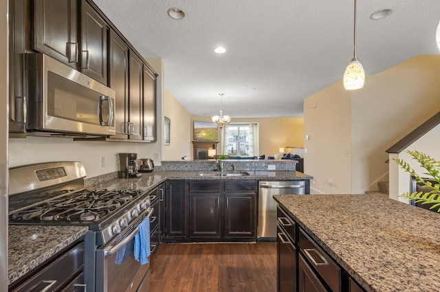 kitchen featuring stainless steel appliances, dark wood-type flooring, a sink, dark brown cabinets, and dark stone counters