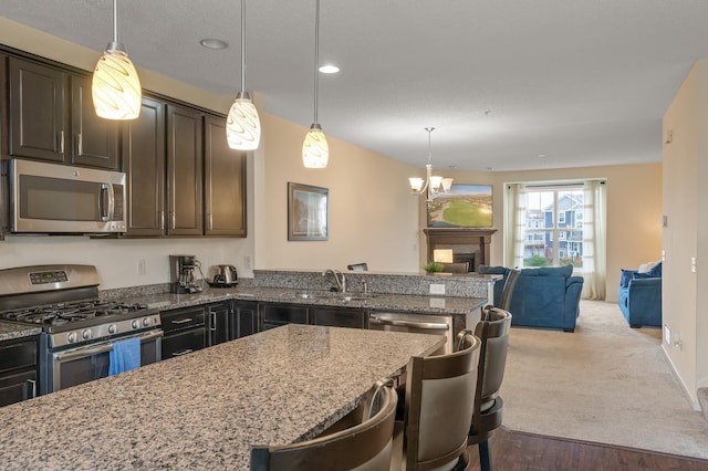 kitchen featuring a fireplace, stainless steel appliances, a sink, dark brown cabinets, and light stone countertops