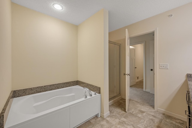 bathroom with a stall shower, a textured ceiling, baseboards, and a bath