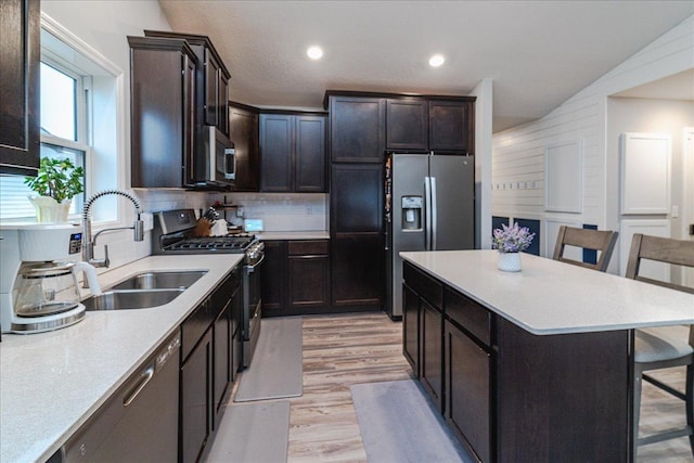 kitchen with appliances with stainless steel finishes, a kitchen breakfast bar, light countertops, light wood-type flooring, and a sink