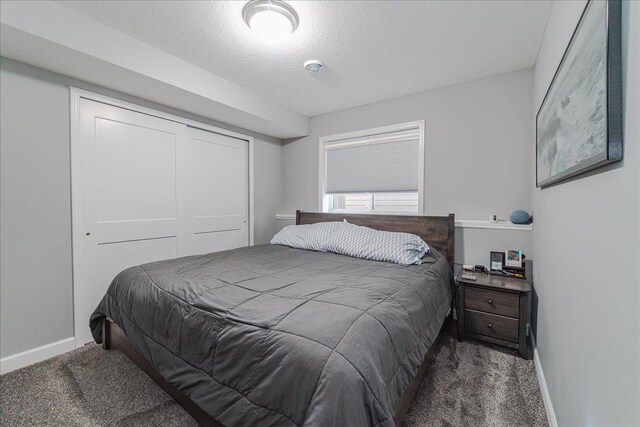 carpeted bedroom featuring a textured ceiling, baseboards, and a closet