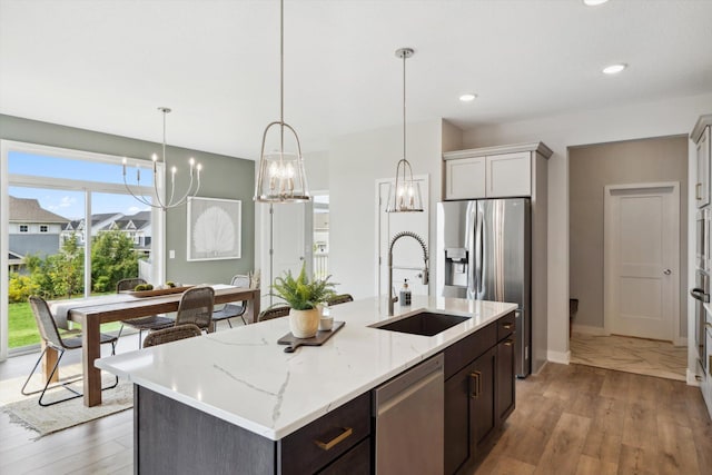 kitchen with hanging light fixtures, a kitchen island with sink, stainless steel appliances, light wood-style floors, and a sink