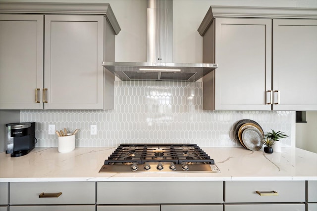 kitchen featuring decorative backsplash, wall chimney exhaust hood, light stone counters, gray cabinets, and stainless steel gas cooktop