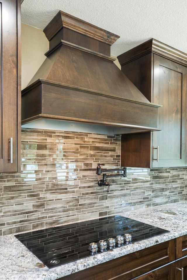 kitchen with a textured ceiling, tasteful backsplash, light stone counters, and dark brown cabinetry