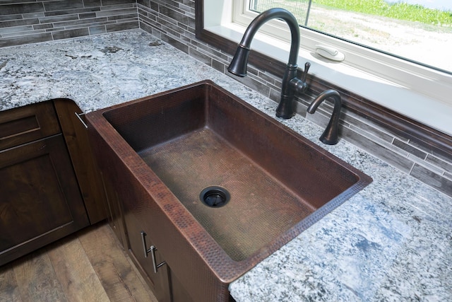 details with light stone counters, dark brown cabinetry, wood finished floors, a sink, and backsplash