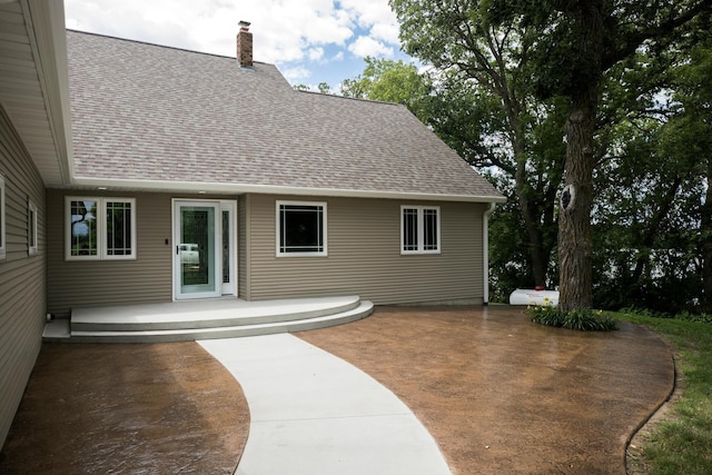 back of house with a patio area, a chimney, and roof with shingles