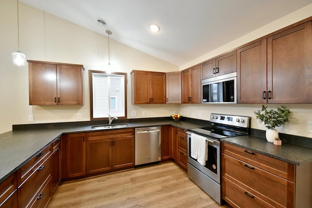 kitchen featuring stainless steel appliances, dark countertops, lofted ceiling, light wood-style floors, and a sink