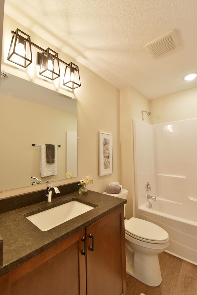 full bath featuring visible vents, toilet, wood finished floors, a textured ceiling, and vanity