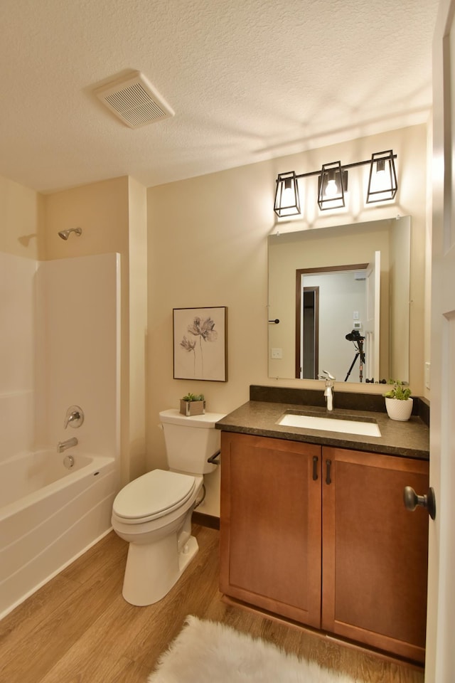 full bathroom with visible vents, toilet, wood finished floors,  shower combination, and a textured ceiling