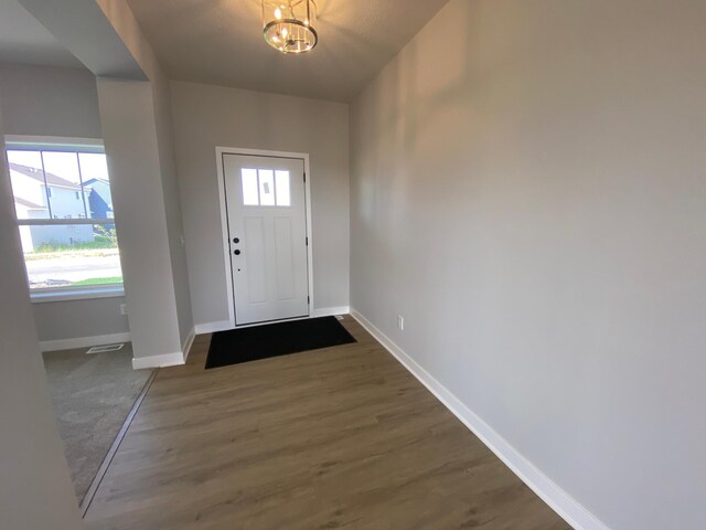 foyer with a notable chandelier, visible vents, baseboards, and wood finished floors