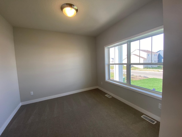 spare room featuring baseboards, visible vents, and dark colored carpet