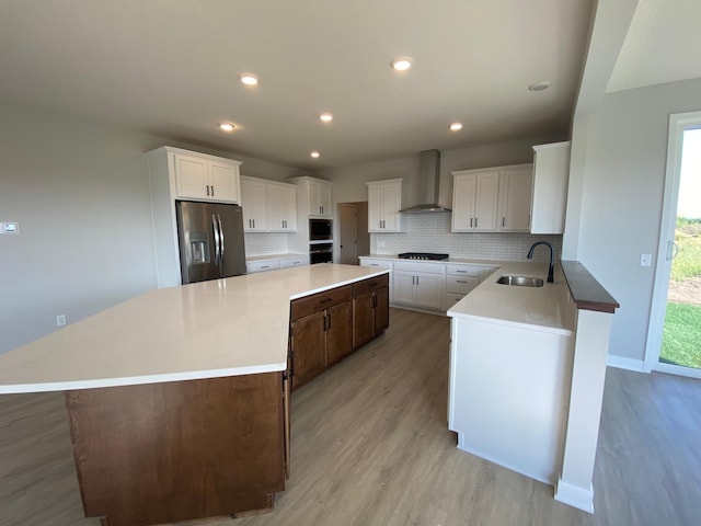 kitchen featuring a spacious island, stainless steel fridge with ice dispenser, backsplash, a sink, and wall chimney exhaust hood