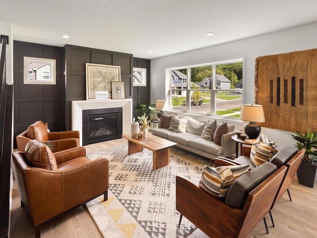 living room with light wood-style flooring, a decorative wall, a glass covered fireplace, and recessed lighting