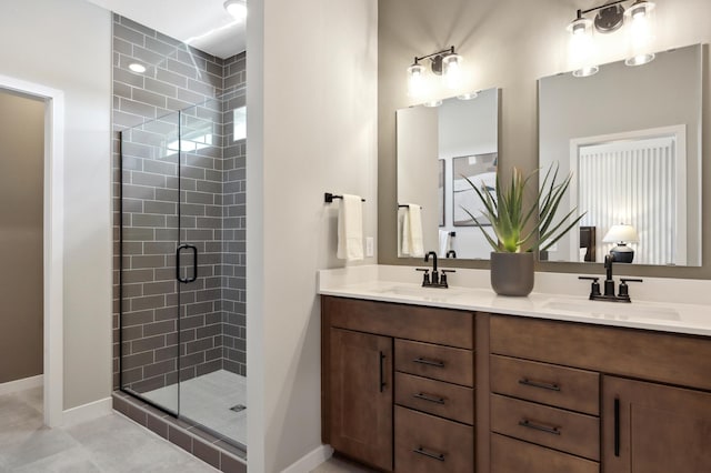 full bathroom with double vanity, a stall shower, baseboards, and a sink