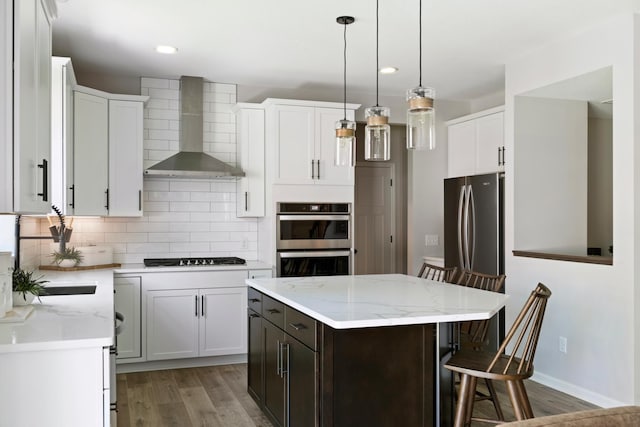 kitchen featuring a breakfast bar, light wood-style floors, appliances with stainless steel finishes, backsplash, and wall chimney exhaust hood