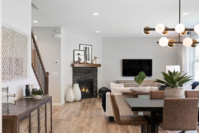 dining space with an inviting chandelier, stairs, light wood-type flooring, a fireplace, and recessed lighting