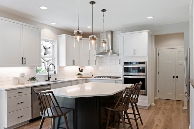 kitchen with wall chimney exhaust hood, light wood-style flooring, appliances with stainless steel finishes, a kitchen breakfast bar, and a sink