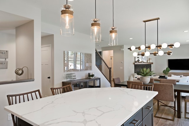 kitchen with open floor plan, light stone counters, wood finished floors, and decorative light fixtures