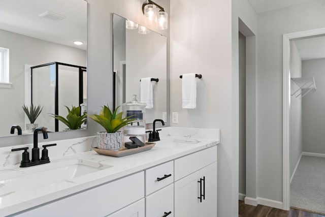 bathroom with double vanity, a stall shower, baseboards, and a sink