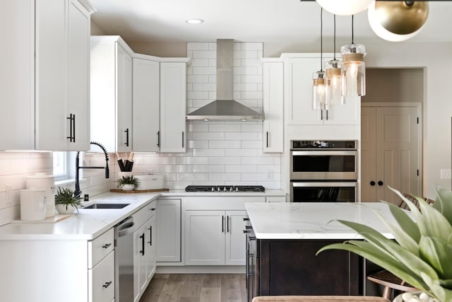 kitchen featuring stainless steel appliances, decorative backsplash, a sink, wall chimney range hood, and light stone countertops