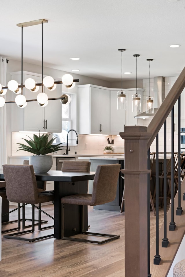 kitchen with white cabinetry, light countertops, light wood-type flooring, backsplash, and decorative light fixtures