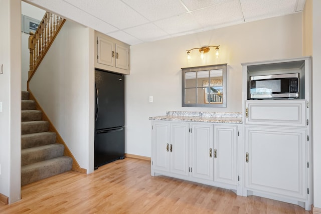 kitchen with stainless steel microwave, light stone counters, light wood-style flooring, freestanding refrigerator, and a paneled ceiling