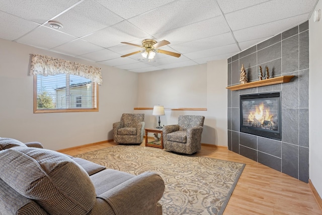 living area with visible vents, a tiled fireplace, a drop ceiling, wood finished floors, and a ceiling fan