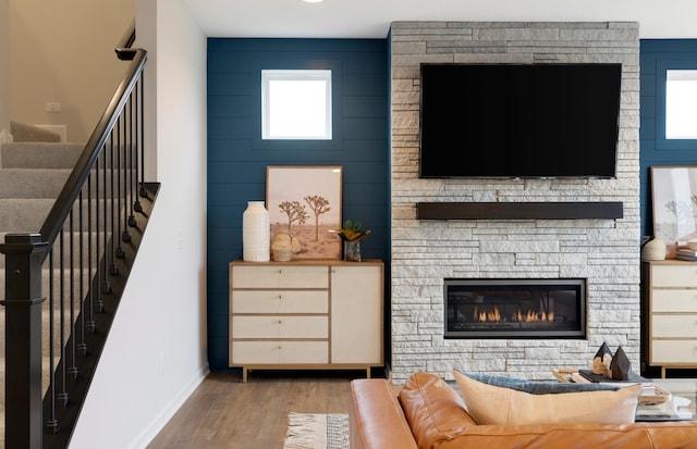 living area featuring baseboards, stairway, wood finished floors, and a stone fireplace