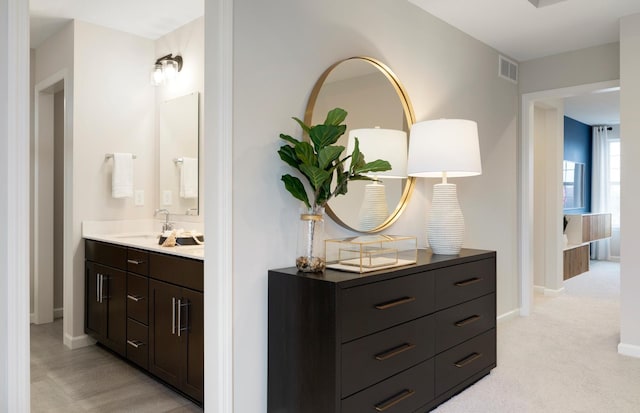 hallway featuring light carpet, a sink, visible vents, and baseboards