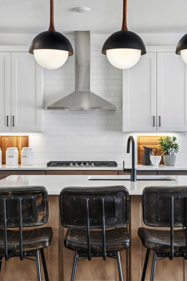 kitchen featuring wall chimney exhaust hood, tasteful backsplash, light countertops, and a kitchen breakfast bar