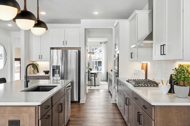 kitchen with dark wood-style floors, light countertops, appliances with stainless steel finishes, a sink, and wall chimney exhaust hood