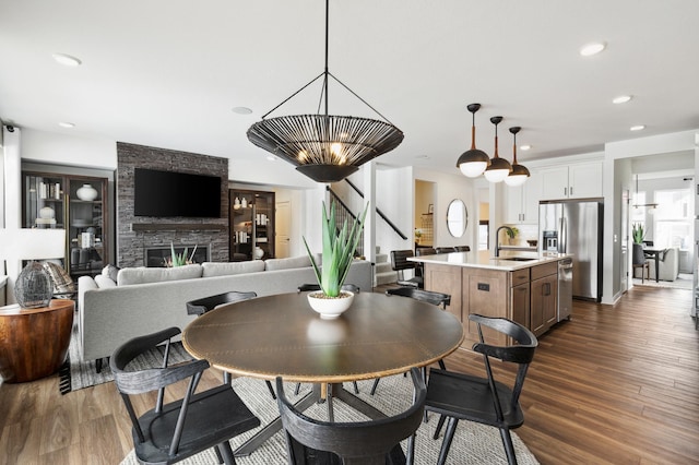 dining area featuring dark wood-type flooring, recessed lighting, a stone fireplace, and stairs