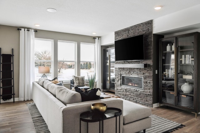 living area featuring a fireplace, a textured ceiling, baseboards, and wood finished floors