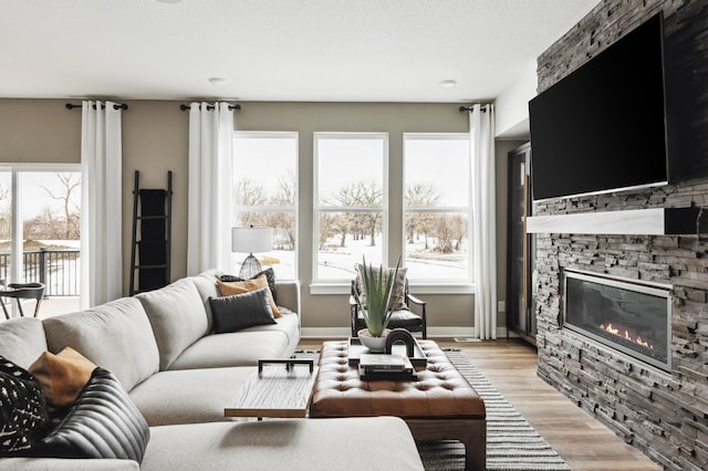 living room featuring light wood-style floors, a healthy amount of sunlight, a stone fireplace, and baseboards