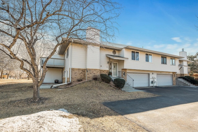 raised ranch with a garage, driveway, a chimney, and brick siding