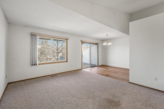 carpeted spare room with baseboards, a textured ceiling, visible vents, and a notable chandelier