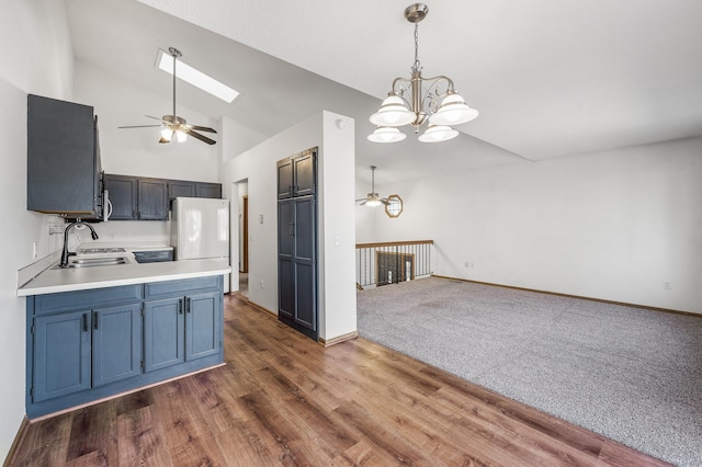 kitchen featuring light countertops, freestanding refrigerator, a sink, a peninsula, and ceiling fan with notable chandelier